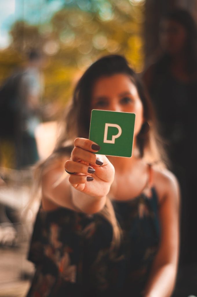 A woman holds a card with a prominent P symbol outdoors, featuring blurred background.